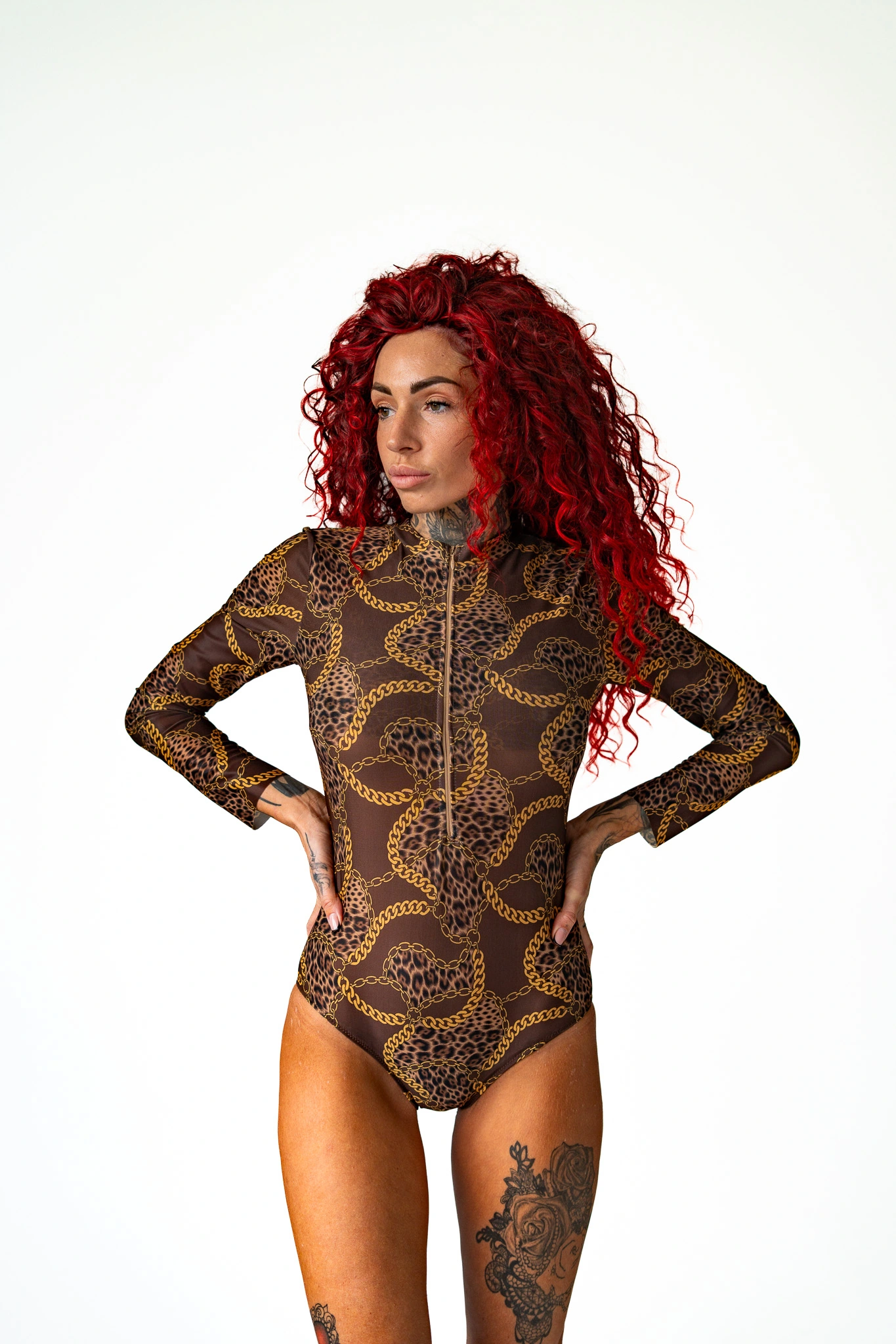 Woman with red curly hair posing sideways in a brown leopard print long-sleeve swimsuit with gold chains Woman with red curly hair posing sideways in a brown leopard print long-sleeve swimsuit with gold chains