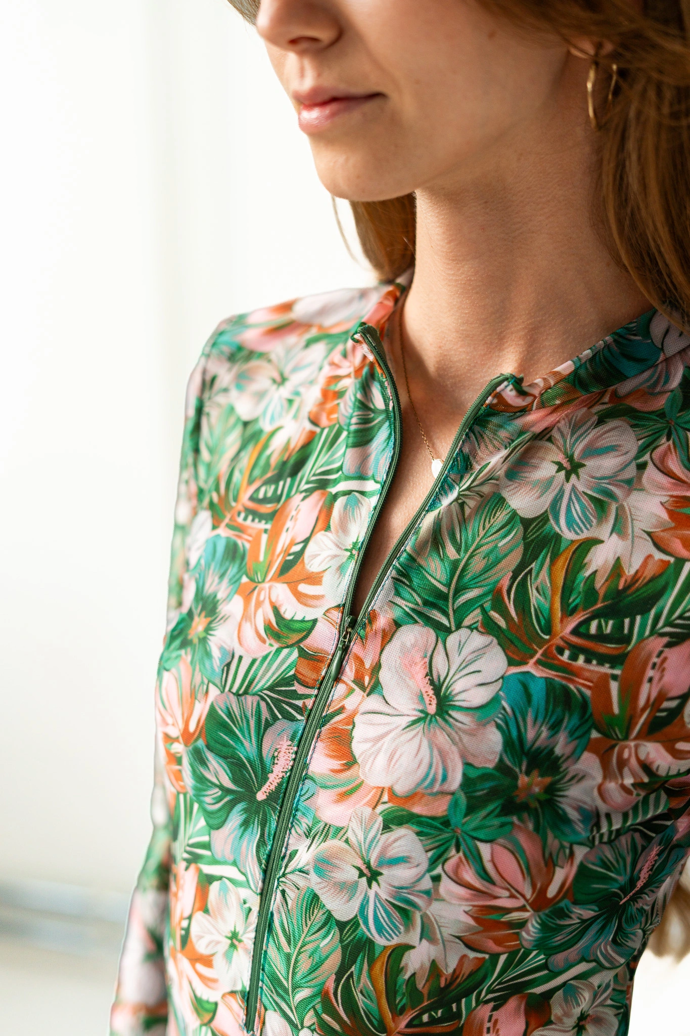 Close-up of the collar and zip of a long-sleeve swimsuit with green tropical hibiscus print Close-up of the collar and zip of a long-sleeve swimsuit with green tropical hibiscus print